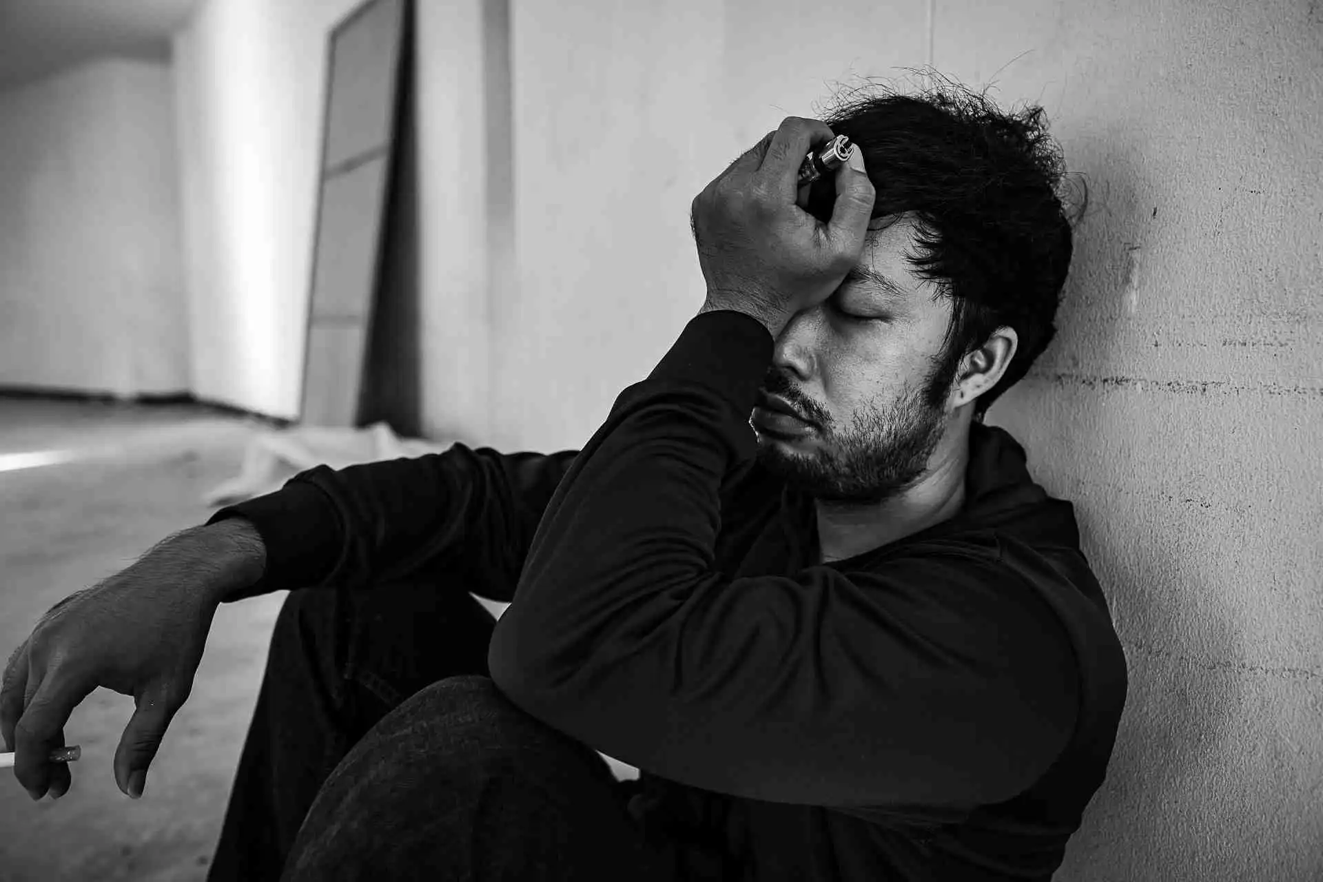 Man sitting against a wall holding his head during a substance abuse self-evaluation